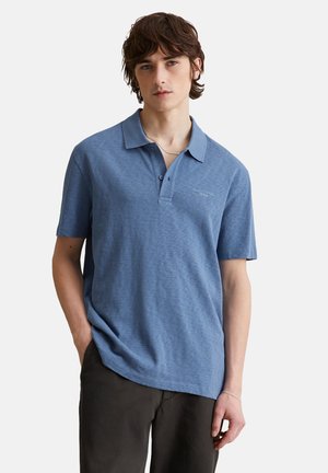 Blaues Poloshirt aus strukturiertem Stoff, mit Kragen und kurzen Ärmeln. Logo auf der Brust gestickt, kombiniert mit dunklen Hosen.