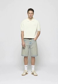 Polo de crema con mangas cortas, pantalones cortos de mezclilla azul claro, zapatillas de crema y calcetas blancas. Estilo casual, ajuste relajado con detalles sutiles.