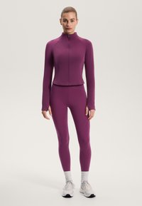Fialová atletická bunda na zip s dlouhými rukávy a odpovídající legíny. Hladká, pružná látka s texturovanými švy a přiléhavým střihem.