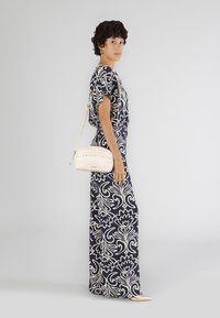 Abito maxi con grande stampa floreale bianca su sfondo blu navy. Accompagnato da una borsa a tracolla color crema con borchie decorative. Texture liscia.