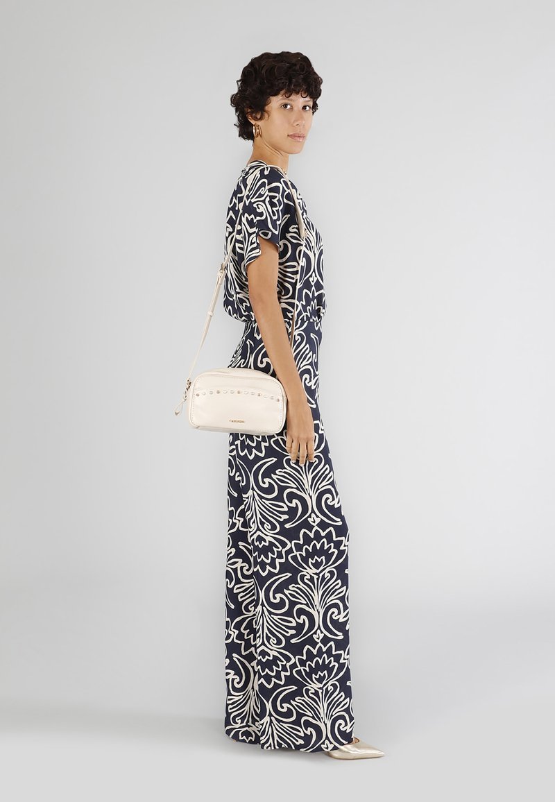 Abito maxi con grande stampa floreale bianca su sfondo blu navy. Accompagnato da una borsa a tracolla color crema con borchie decorative. Texture liscia.