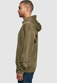 Olive green hoodie with a kangaroo pocket, ribbed cuffs, and hem. The fabric has a soft texture, featuring a subtle design on the front.