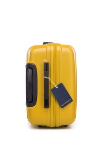 Žlutý kufr s tvrdou skořápkou, černé rukojeti a tmavě modrá visačka na zavazadlo s nápisem "WITTCHEN" na bílém pozadí.