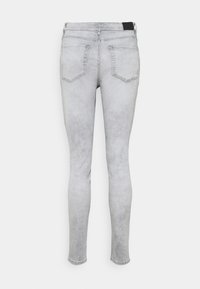Vaqueros skinny gris claro con bolsillos traseros, exhibidos contra un fondo blanco liso.