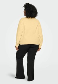 Kollane kootud kampsun lõdva istuvuse, ümarate kaeluse ja soonikkoes mansettidega, mis on kombineeritud tihedalt istuvate mustade pükstega. Sujuv tekstuur, vabaaja stiil.