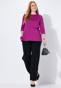 Magenta longsleeve top met beaded details bij de hals, gecombineerd met zwarte wijde broek en een zwart handtas met pailletten.