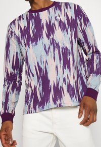 Chemise à manches longues présentant un motif abstrait violet, bleu et rose. Fabriquée en matériau doux avec des poignets et un col côtelés.