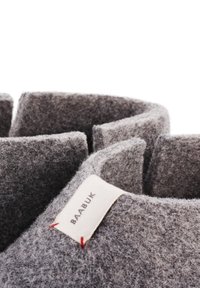 Šedé plstěné pantofle s texturovaným povrchem, mají zakřivený design a štítek s nápisem "BAABUK" a červeným prošíváním.