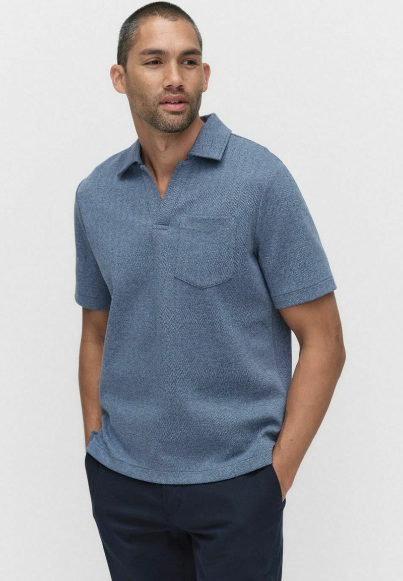 Puva-paita sinisessä (herringbone) kudoksessa, lyhyet hihat, lovella varustettu kaulus, yksi rintatasku, valmistettu teksturoidusta kankaasta.