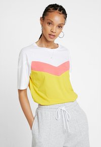 Camiseta de manga corta con la parte superior blanca, la parte inferior amarilla y diseño de chevron rosa. Hecha de algodón suave, presenta un ajuste relajado y escote redondo.