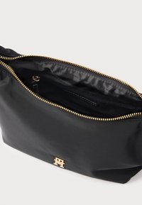 Pochette en nylon noir avec une fermeture éclair et des accessoires en métal doré. L'intérieur comprend une doublure texturée et une poche zippée. Affiche un logo bien visible.