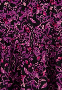 Květinová látka v purpurové a růžové barvě na černém pozadí má stažený detail kolem pasu se zkrouceným okrajem.