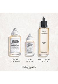 Trzy flakoniki perfum Maison Margiela Replica Beach Walk w rozmiarach 100 ml, 30 ml oraz 100 ml uzupełnienia na jasnej powierzchni.