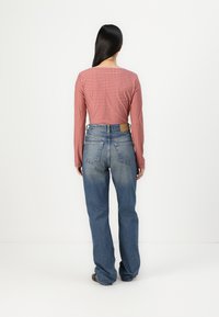 Röd och vit rutigt långärmad topp i kombination med högmidjade blå jeans. Jeansarna är något utsvängda med en blekt finish.