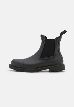 Botas de borracha pretas até ao tornozelo com painéis laterais elásticos, alça de puxar e sola texturizada, apresentando um detalhe em tiras com um pequeno logotipo.