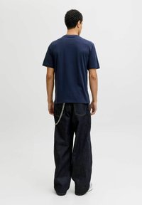Camiseta de algodón azul marino de manga corta, combinada con pantalones anchos de mezclilla oscura que presentan detalles de cadena y un prominente pespunte.