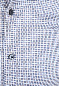 Blaues und beiges geometrisches Muster auf einem Hemdenstoff mit zwei sichtbaren schwarzen Knöpfen entlang der Naht.