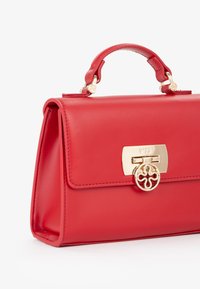 Sac à main en cuir rouge au design épuré, avec des accessoires en or et un verrou décoratif. Dispose d'une courte anse supérieure et d'une texture lisse.
