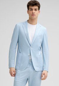 Helles blaues Blazer aus strukturierter Stoff, mit Reverskragen, zwei Vorderaschen und Knopfverschluss, getragen über einem weißen Hemd.