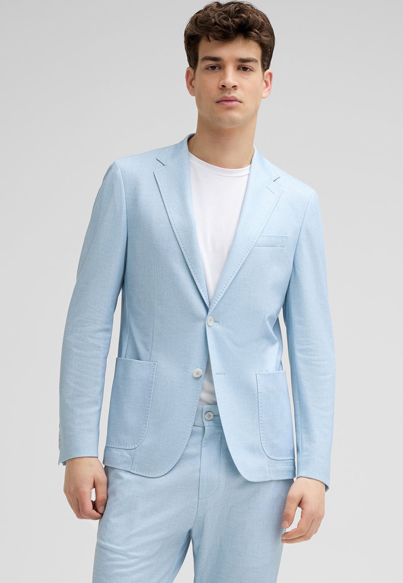 Helles blaues Blazer aus strukturierter Stoff, mit Reverskragen, zwei Vorderaschen und Knopfverschluss, getragen über einem weißen Hemd.