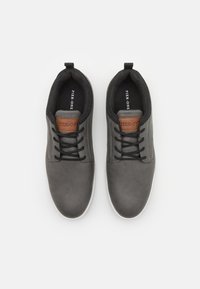 Chaussures en cuir gris avec des lacets noirs et une accentuation marron sur la languette. Semelle plate, bout arrondi et doublure intérieure texturée.