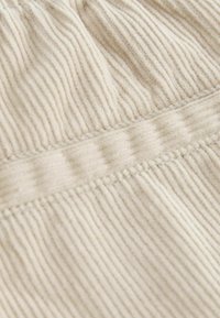 Primer plano de tela beige acanalada con detalle de costura horizontal, mostrando una textura suave y sombras sutiles.