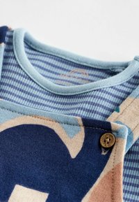 Katoenen kleding met een blauw gestreepte halslijn, voorzien van een grafisch ontwerp in beige, marineblauw en teal, en een decoratieve bruine knop.
