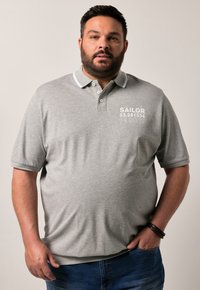 Šedé polo tričko s bílým límečkem, s nápisem 'SAILOR 53.281534 N 2007' v bílé barvě na levé straně. Krátké rukávy a uvolněný střih.