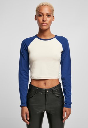Haut à manches longues coupé en crème avec des manches raglan bleues, fabriqué en tissu doux. Présente un col rond et un ourlet élastique.