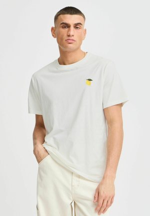 Light cream T-shirt made of soft cotton, featuring a small yellow lemon and green leaf embroidery on the left chest. Round neckline, short sleeves.