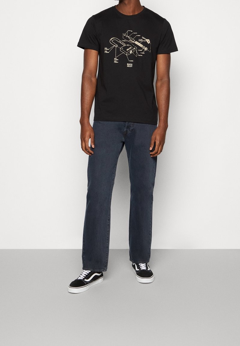 Svart t-shirt med en teknisk ritningsdesign i beige, kombinerad med mörka jeans och svarta Vans-skor. Avslappnad passform och korta ärmar.