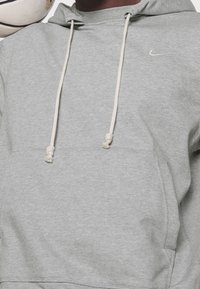 Sweat à capuche Nike gris avec une texture douce, cordons de serrage ajustables et un petit logo blanc sur la poitrine gauche. Design simple, poche kangourou.