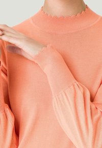 Katoenen pullover in zacht koraal, met een geschulpte hoge halslijn en geraffineerde mouwen. Glad textiel met geribbelde accenten bij de manchetten en kraag.