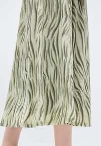 Κατώτερα πόδια που φοράνε μια ροή φούστα με πράσινες και μπεζ ρίγες, παρόμοιες με ζέβρες, σε απλό λευκό φόντο.