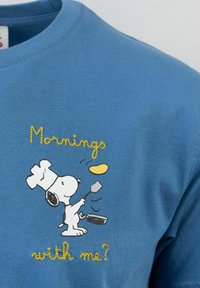 T-shirt blu in cotone con una grafica di un cane dei cartoni animati in cappello da chef che tiene una spatola, con testo ricamato giallo che dice "Mattine con me?"