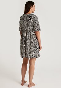 Abito con motivo di foglie di palma in bianco e nero, con maniche corte e vita aderente, che arriva a metà coscia, realizzato in un tessuto leggero.