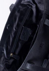 Black leather handbag interior with a zip pocket, smooth lining, embossed logo pattern, and magnetic snap closure.