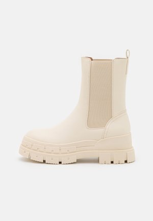 Beige chunky Chelsea-støvle med elastisk sidespanel, trækstrop bagpå og tyk sål med groft mønster for ekstra greb og stil.