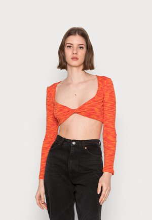 Top cropped riscado vermelho e laranja com mangas longas e design de frente torcido, combinado com jeans pretos de cintura alta. Textura suave.