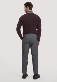 Bordeauxfarbenes Sweatshirt mit rundem Halsausschnitt über einem karierten Hemd, kombiniert mit hellgrauen maßgeschneiderten Hosen und schwarzen Schuhen, von hinten betrachtet.