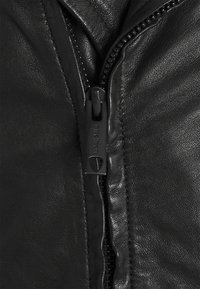 Detail van een zwarte leren jas met een rits voorzien van een trekker met merklogo. De textuur is glad, met zichtbare stiksels langs de naden.