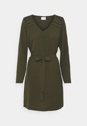 Vihreä oliivinvihreä mekko pitkillä hihoilla, V-pääntiellä ja vyötäröllä samasta kankaasta valmistettu vyö. Mekossa on teksturoituja hartiakoristeita.