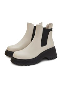 Botines de cuero beige con paneles laterales elásticos negros, suela de goma texturizada negra y un tacón ancho.