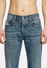 Blue denim jeans with a faded finish, five-pocket design, and a button closure. Features frayed edges on the front pockets.