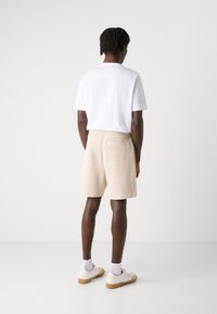 Shorts texturés beiges clairs avec une taille élastique et une poche arrière, associés à un t-shirt blanc uni à manches courtes et des baskets blanches.