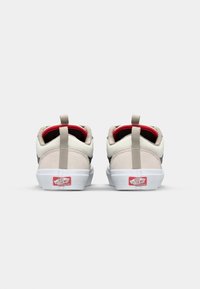 Sneakers med overdel i beige semsket skinn, svarte detaljer og hvite gummisåler. Har røde fôr og hælløkker. Logo på hælen.
