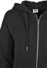 Čierna mikina na zips vyrobená z bavlnenej zmesi. Má fleecovú textúru, predné vrecká a nastaviteľné šnúrky na kapucni. Strieborný zips ako detail.