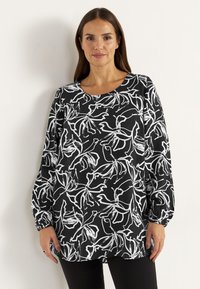Svart långärmad topp med ett vitt blommönster. Rund halsringning och ärmarna är samlade vid handlederna. Mjuk tygkänsla.