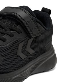 Czarne buty sportowe z siateczkową cholewką, wyściełanym kołnierzem, paskiem na rzep oraz teksturowaną podeszwą z charakterystycznym ukośnym wzorem akcentującym.