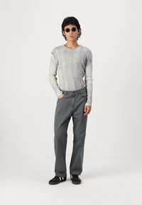 Siva rebrasta majica dugih rukava, smešne sunčane naočale, sivi pantaloni i crne patike. Outfit se odlikuje ležernim krojem i minimalističkim dizajnom.